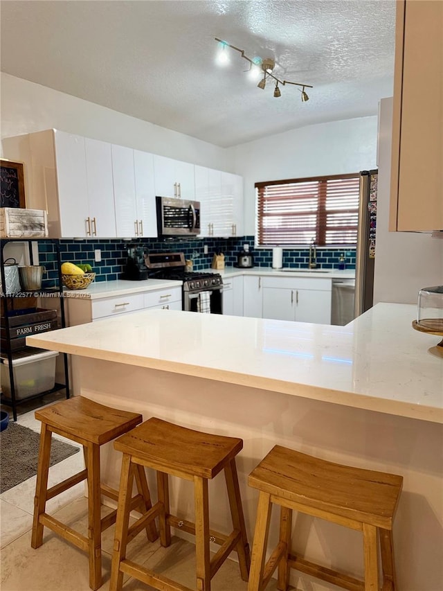 kitchen featuring white cabinets, a kitchen bar, kitchen peninsula, and appliances with stainless steel finishes