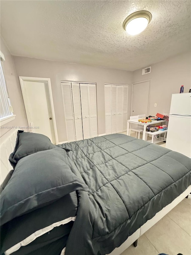 bedroom with white fridge, a textured ceiling, and two closets