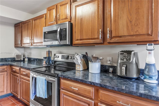 kitchen with stainless steel appliances, tile patterned floors, and dark stone counters