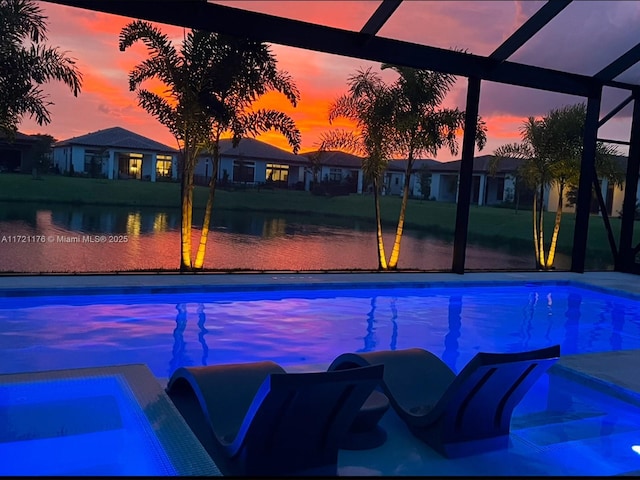 pool at dusk featuring glass enclosure and a hot tub