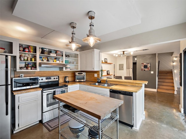 kitchen with hanging light fixtures, butcher block counters, white cabinets, appliances with stainless steel finishes, and sink