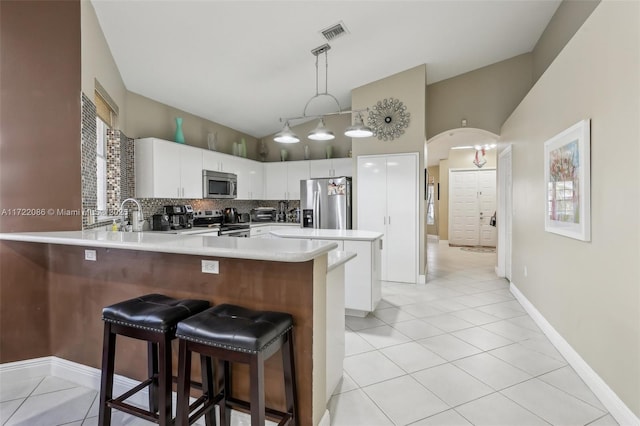 kitchen featuring lofted ceiling, kitchen peninsula, decorative light fixtures, white cabinetry, and stainless steel appliances