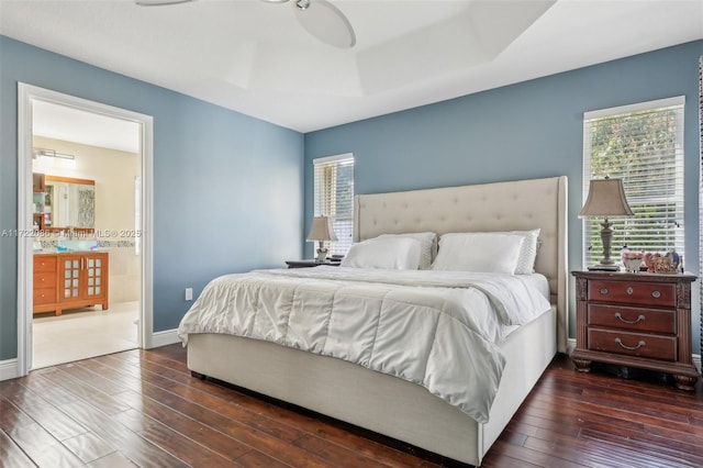 bedroom with ensuite bathroom, dark hardwood / wood-style floors, and a raised ceiling