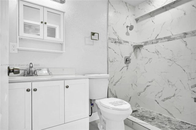 bathroom featuring a tile shower, vanity, and toilet