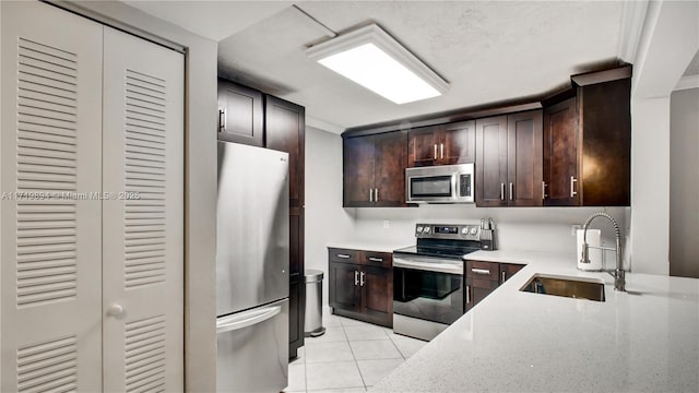 kitchen with appliances with stainless steel finishes, light tile patterned floors, sink, dark brown cabinets, and light stone counters