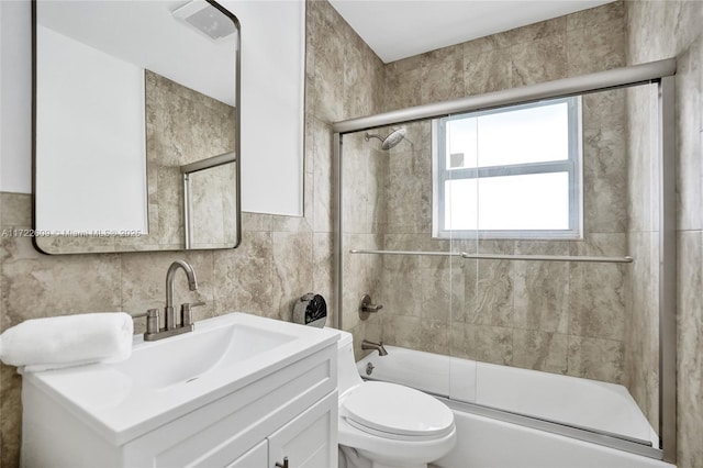 full bathroom with combined bath / shower with glass door, tile walls, vanity, tasteful backsplash, and toilet