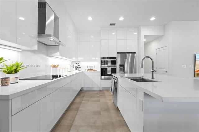 kitchen featuring white cabinets, wall chimney exhaust hood, a center island with sink, and stainless steel appliances