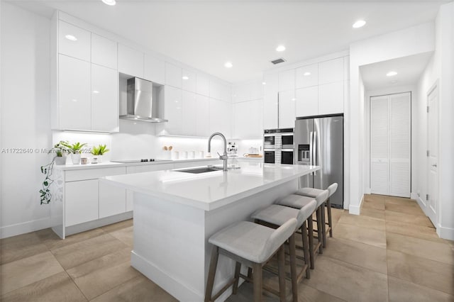 kitchen featuring appliances with stainless steel finishes, a kitchen breakfast bar, wall chimney exhaust hood, sink, and an island with sink