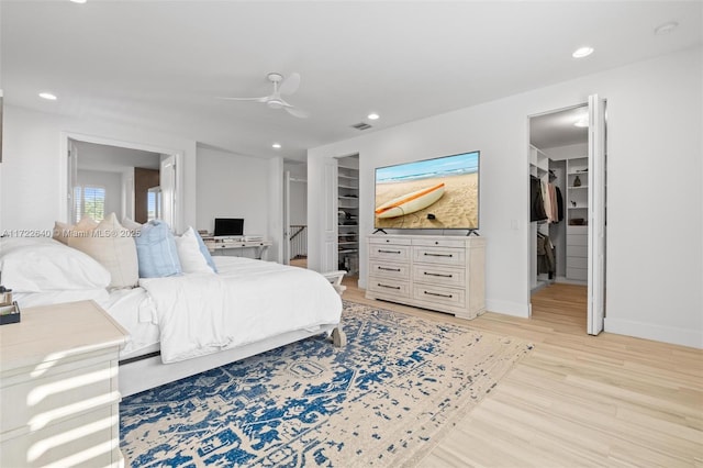 bedroom with a walk in closet, a closet, light hardwood / wood-style flooring, and ceiling fan