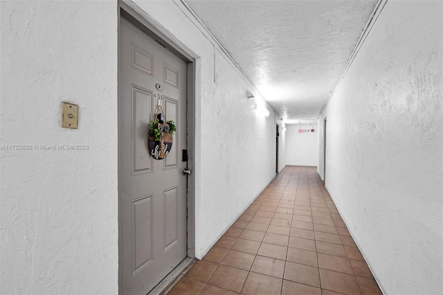 hallway featuring tile patterned floors, crown molding, and a textured ceiling