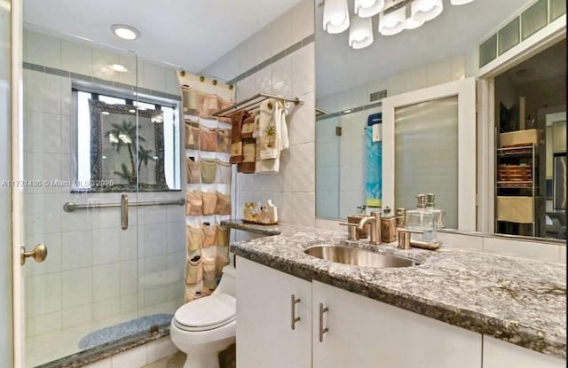 bathroom featuring vanity, toilet, a shower with door, and tile walls