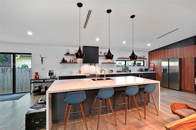 kitchen with backsplash, a kitchen island with sink, light hardwood / wood-style flooring, stainless steel fridge with ice dispenser, and lofted ceiling