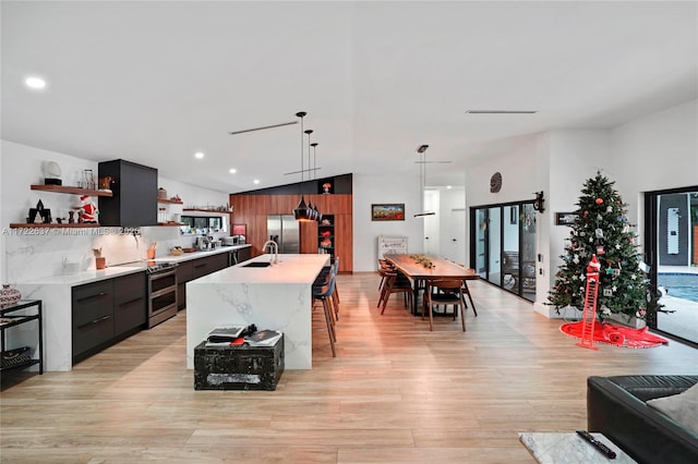 kitchen with stainless steel appliances, sink, decorative light fixtures, a center island with sink, and light hardwood / wood-style flooring