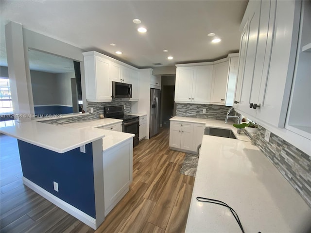 kitchen with kitchen peninsula, a kitchen breakfast bar, black electric range oven, sink, and white cabinetry