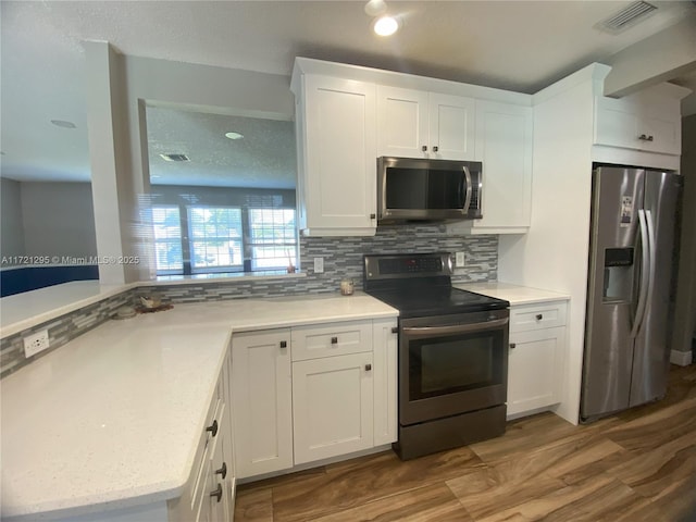 kitchen with light stone countertops, tasteful backsplash, appliances with stainless steel finishes, white cabinets, and hardwood / wood-style flooring