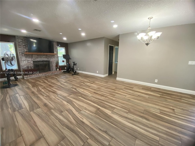 unfurnished living room featuring a chandelier, a fireplace, hardwood / wood-style floors, and a textured ceiling