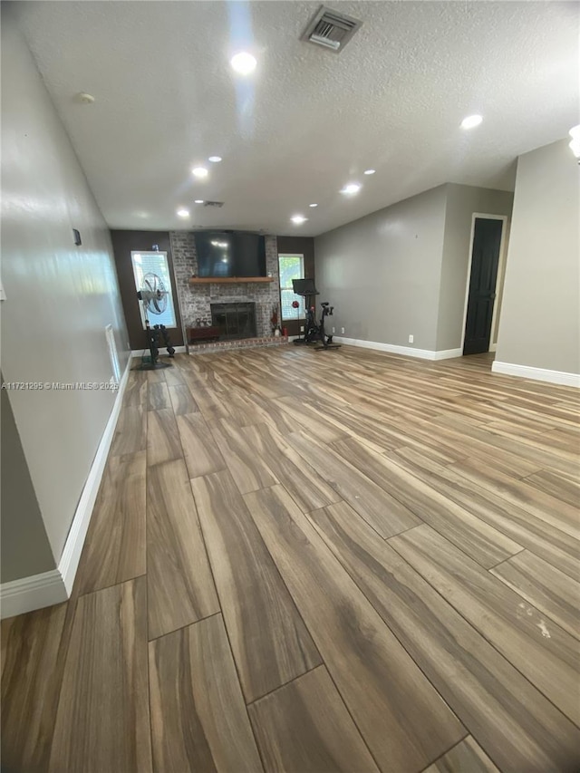 unfurnished living room featuring light hardwood / wood-style floors, a textured ceiling, and a brick fireplace