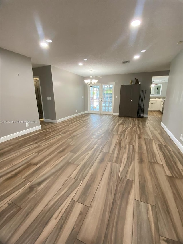 unfurnished living room featuring hardwood / wood-style floors, an inviting chandelier, and french doors