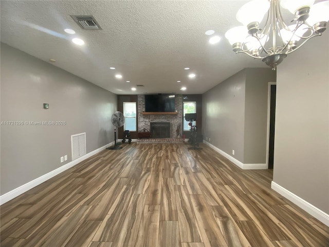 unfurnished living room with a textured ceiling, a chandelier, dark hardwood / wood-style floors, and a brick fireplace