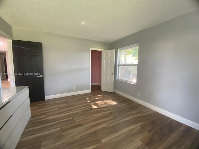 unfurnished bedroom featuring a walk in closet, a closet, dark hardwood / wood-style flooring, and a textured ceiling