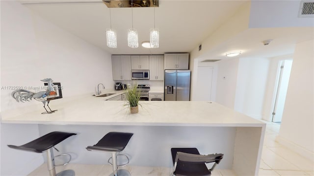 kitchen featuring hanging light fixtures, sink, appliances with stainless steel finishes, a kitchen bar, and kitchen peninsula