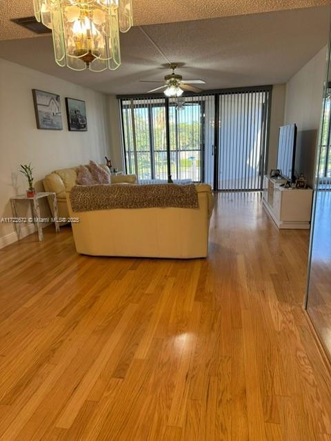 unfurnished living room with light hardwood / wood-style flooring, ceiling fan with notable chandelier, and a textured ceiling