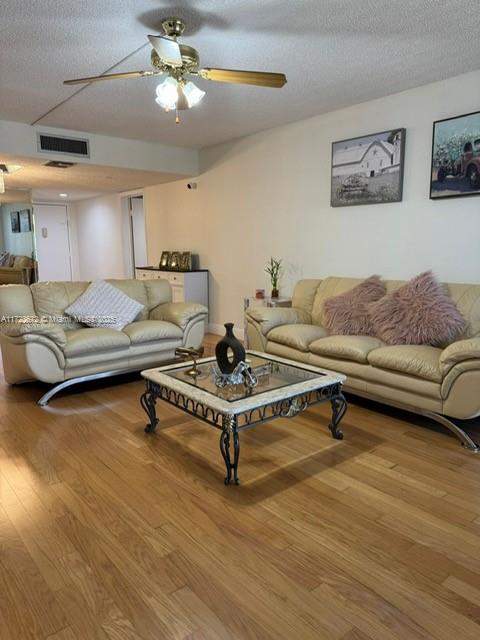 living room with a textured ceiling, hardwood / wood-style flooring, and ceiling fan