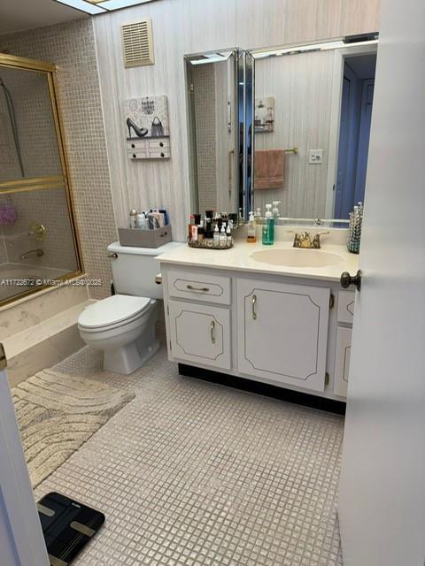 full bathroom with tile patterned flooring, vanity, bath / shower combo with glass door, and toilet