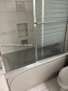 bathroom with tile patterned flooring, combined bath / shower with glass door, and toilet