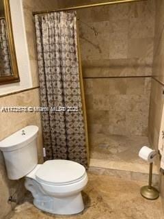 bathroom with walk in shower, toilet, and tile walls