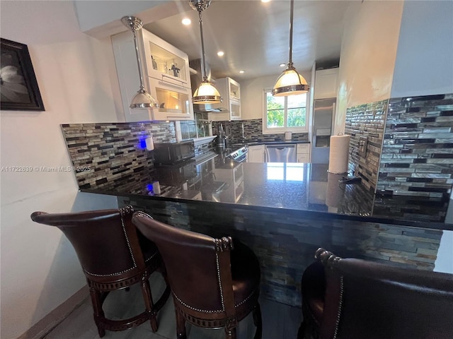 kitchen with white cabinets, appliances with stainless steel finishes, decorative light fixtures, a kitchen bar, and kitchen peninsula