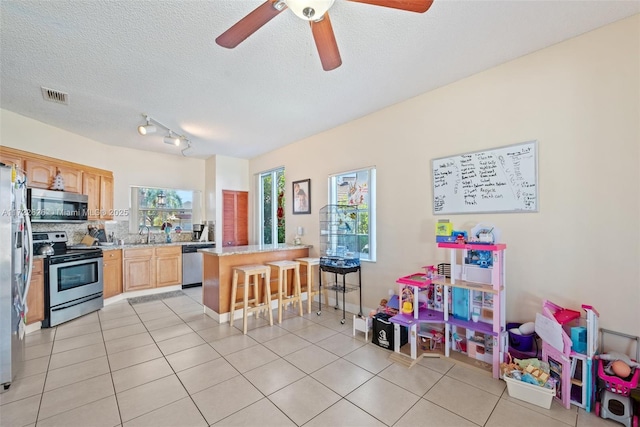 kitchen with stainless steel appliances, light tile patterned floors, ceiling fan, a kitchen bar, and decorative backsplash