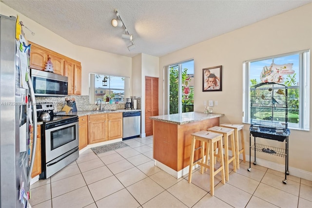 kitchen featuring stainless steel appliances, a kitchen bar, kitchen peninsula, and light stone countertops