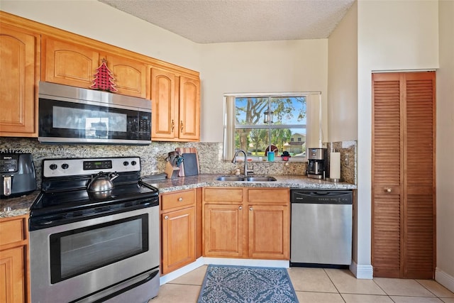 kitchen with sink, tasteful backsplash, light tile patterned floors, appliances with stainless steel finishes, and light stone countertops