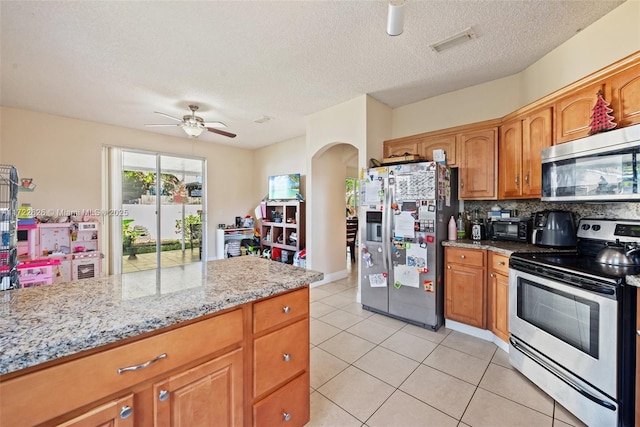 kitchen featuring light tile patterned floors, ceiling fan, appliances with stainless steel finishes, tasteful backsplash, and light stone countertops