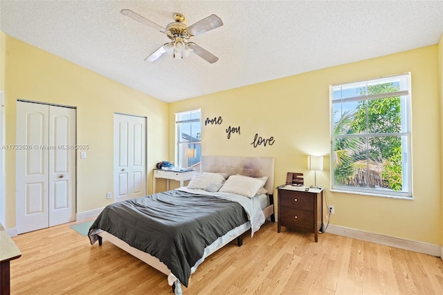 bedroom featuring light hardwood / wood-style floors, ceiling fan, multiple closets, multiple windows, and a textured ceiling