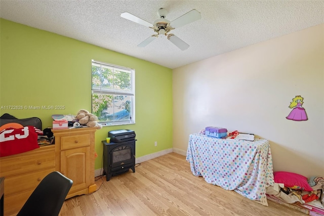 bedroom with ceiling fan, light hardwood / wood-style floors, a textured ceiling, and a wood stove