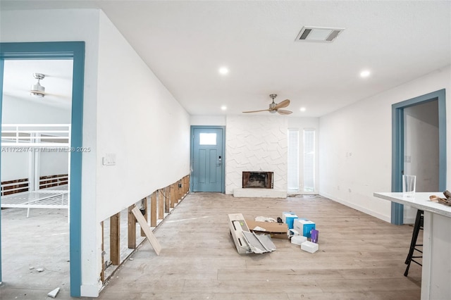 unfurnished living room featuring light hardwood / wood-style flooring, a stone fireplace, and ceiling fan