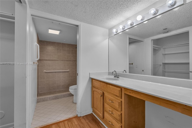 bathroom with hardwood / wood-style flooring, toilet, vanity, and a tile shower