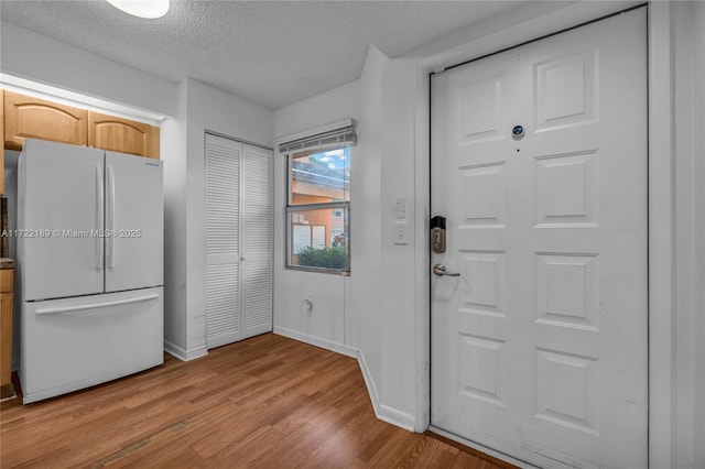 interior space featuring a textured ceiling, light brown cabinetry, light hardwood / wood-style flooring, and white fridge