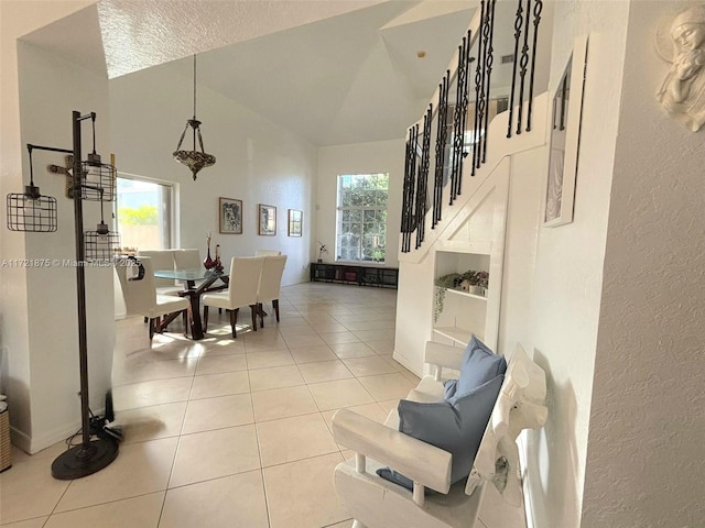 dining space with a textured wall, high vaulted ceiling, light tile patterned flooring, baseboards, and stairway