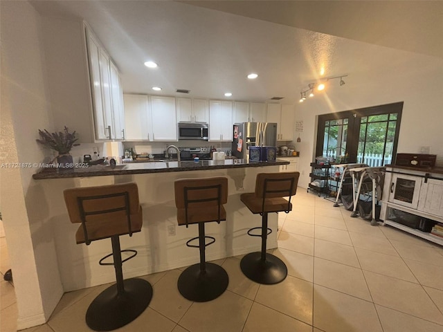 kitchen with a breakfast bar area, stainless steel appliances, dark countertops, white cabinetry, and a peninsula