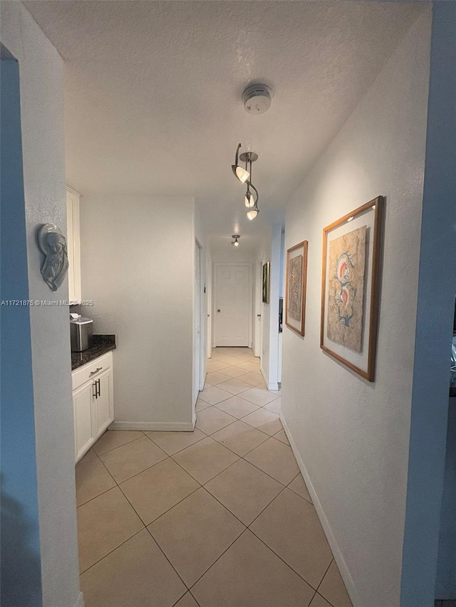 hall with baseboards, a textured ceiling, and light tile patterned flooring