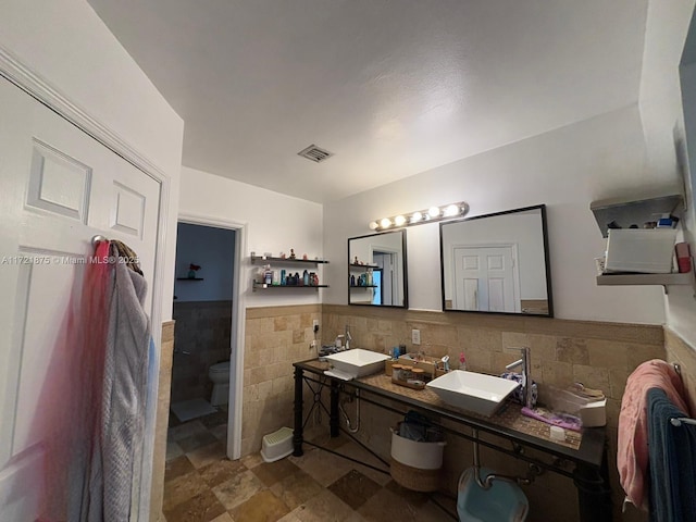 full bathroom featuring visible vents, a wainscoted wall, a sink, and tile walls