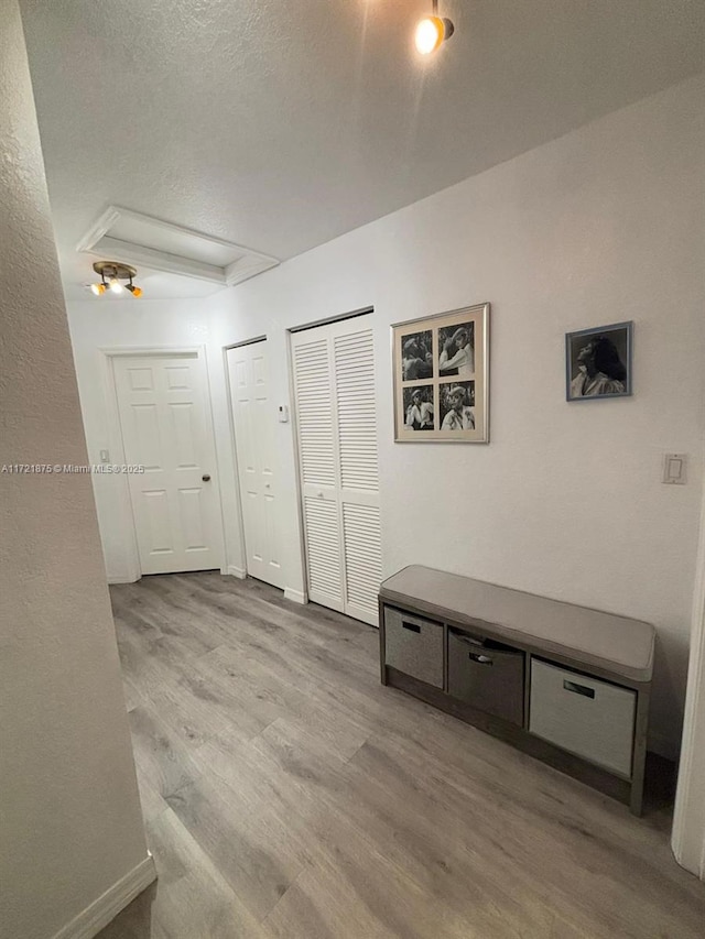 hall with attic access, a textured ceiling, baseboards, and wood finished floors