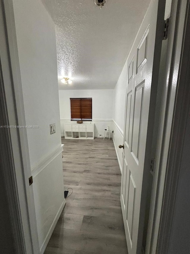 hallway with a textured ceiling and wood finished floors