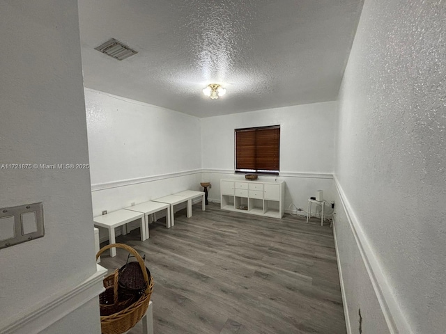 interior space featuring visible vents, a textured wall, a textured ceiling, and wood finished floors