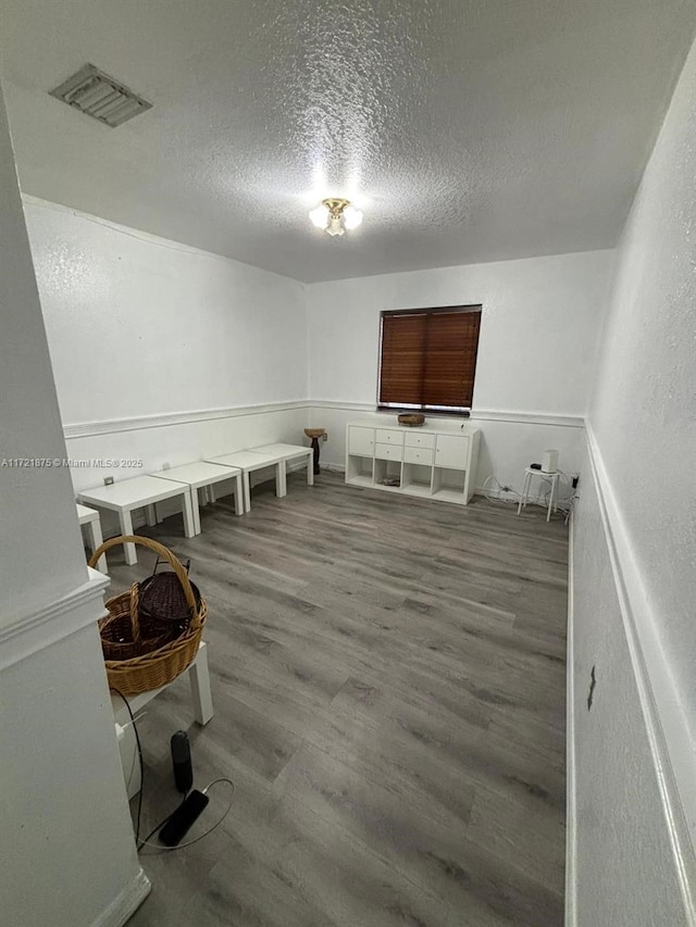 living area with a textured ceiling, visible vents, and wood finished floors