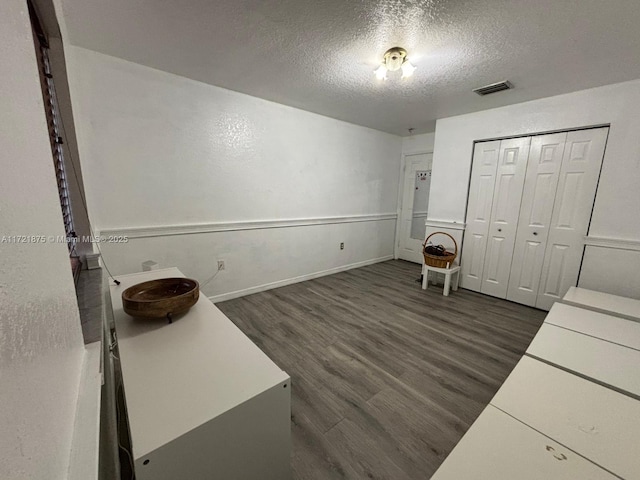 unfurnished office featuring baseboards, visible vents, dark wood finished floors, and a textured ceiling