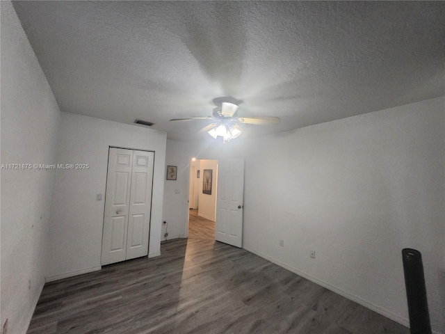 unfurnished room with ceiling fan, a textured ceiling, visible vents, and wood finished floors